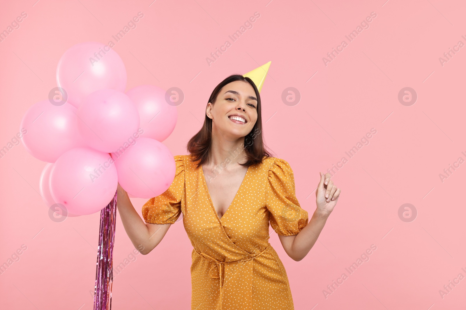 Photo of Happy young woman in party hat with balloons on pink background