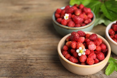 Fresh wild strawberries and flowers in bowls on wooden table. Space for text