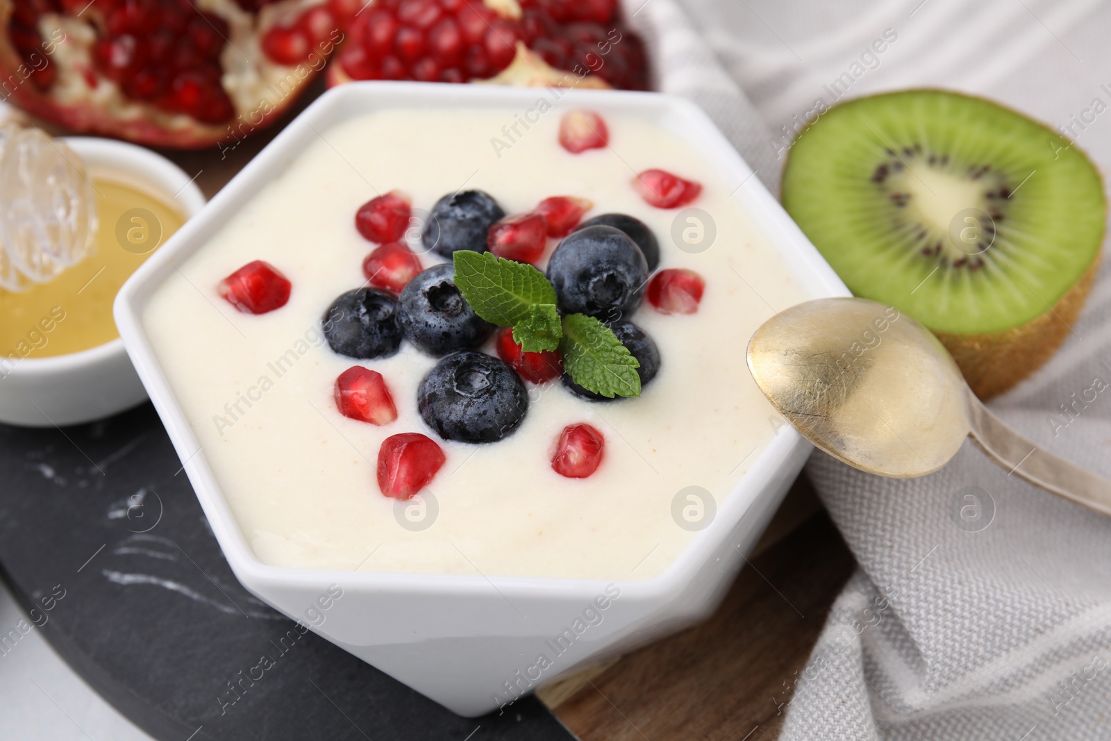 Photo of Bowl of delicious semolina pudding with blueberries, pomegranate and mint served on table, closeup