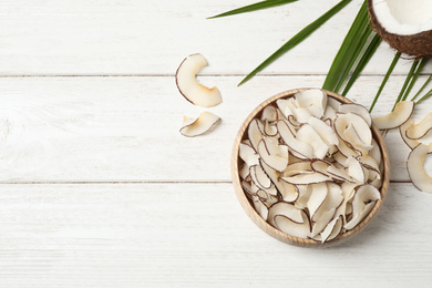 Tasty coconut chips on white wooden table, flat lay. Space for text