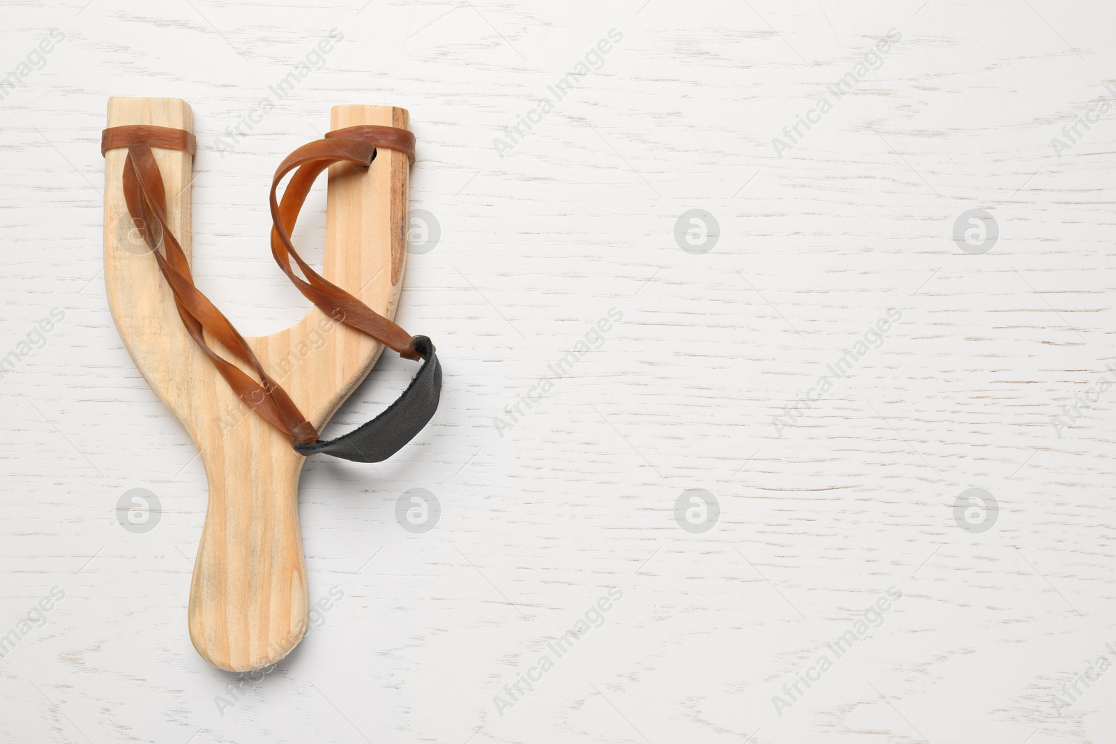 Photo of Slingshot with leather pouch on white wooden background, top view. Space for text