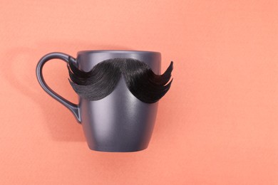 Photo of Man's face made of artificial mustache and cup on pink background, top view. Space for text