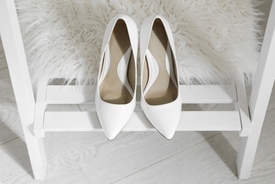 Photo of Pair of white wedding high heel shoes on wooden rack indoors, above view