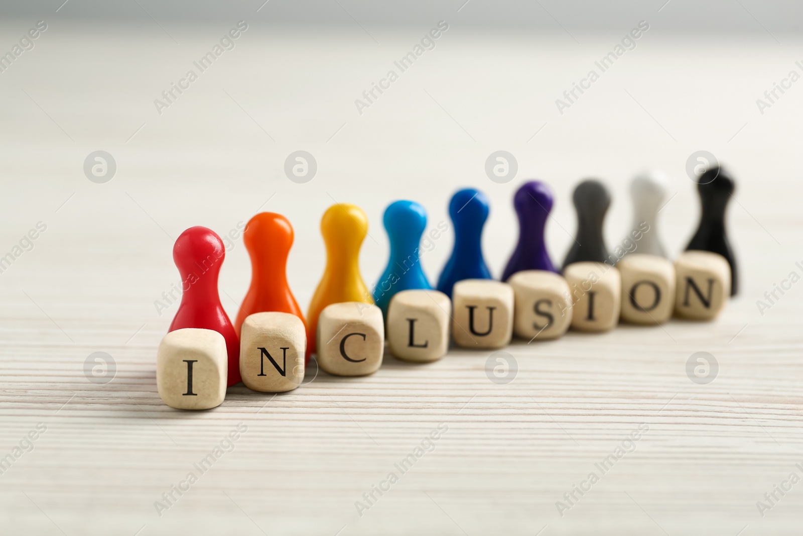 Photo of Colorful pawns and cubes with word Inclusion on white wooden table