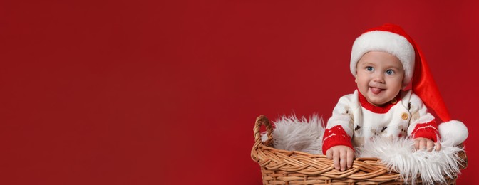 Image of Cute baby in wicker basket on red background, banner design with space for text. Christmas celebration