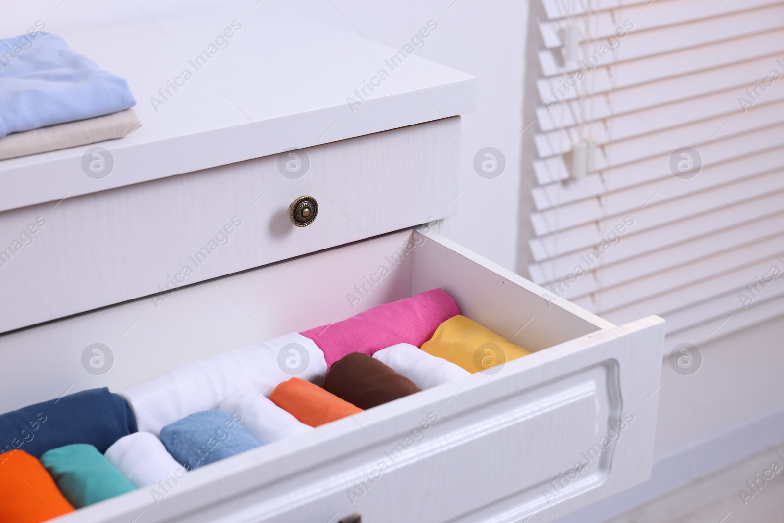 Photo of Open drawer with rolled shirts indoors. Organizing clothes