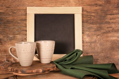 Photo of Ceramic cups on table near small chalkboard