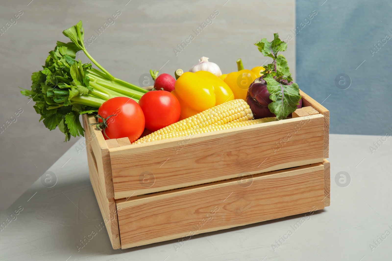 Photo of Wooden crate with fresh vegetables on gray table