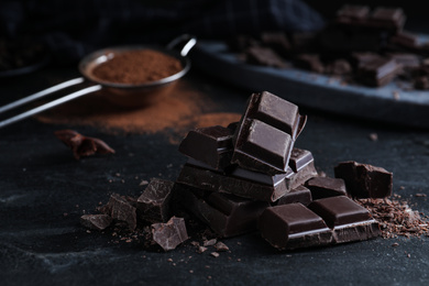 Photo of Pieces of delicious dark chocolate on black table