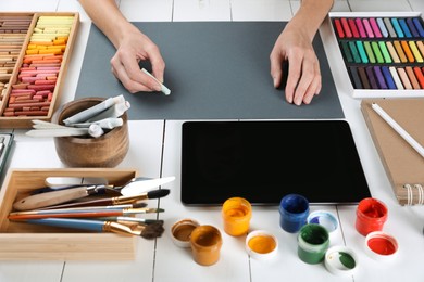 Photo of Artist drawing with chalk pastel on grey paper at white wooden table, closeup