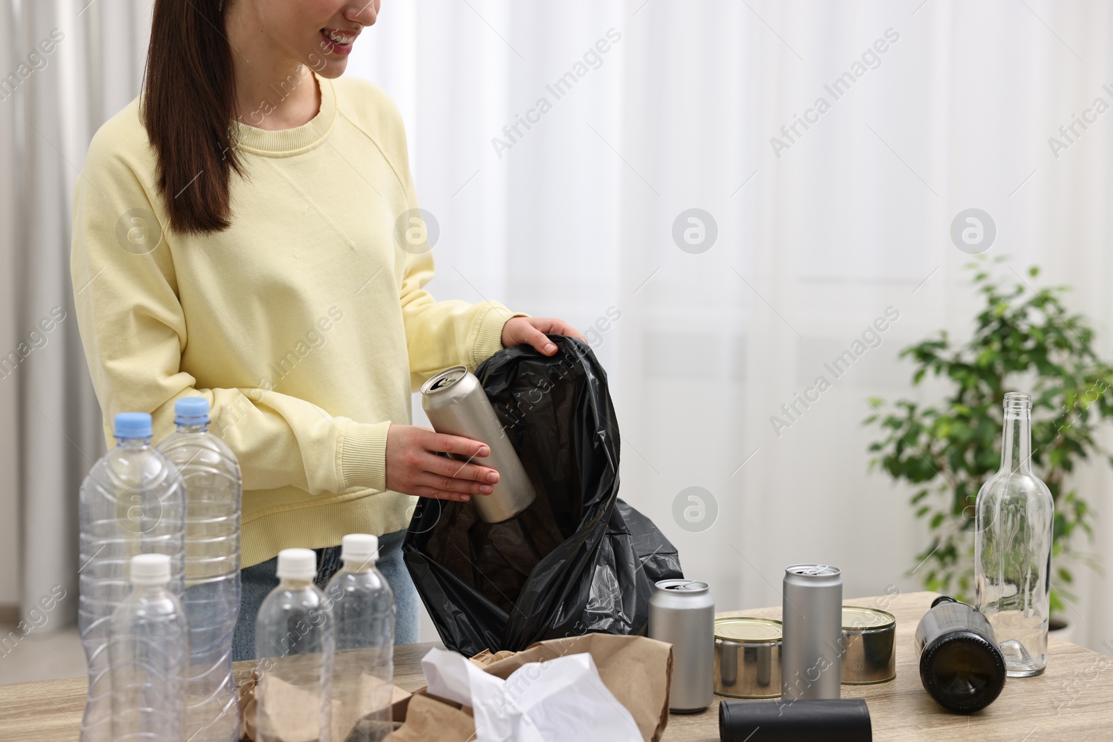 Photo of Smiling woman separating garbage at table in room, closeup