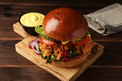 Photo of Delicious burger with crispy chicken patty and sauce on wooden table, closeup