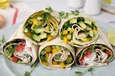 Delicious sandwich wraps with fresh vegetables and slice of lemon on plate, closeup