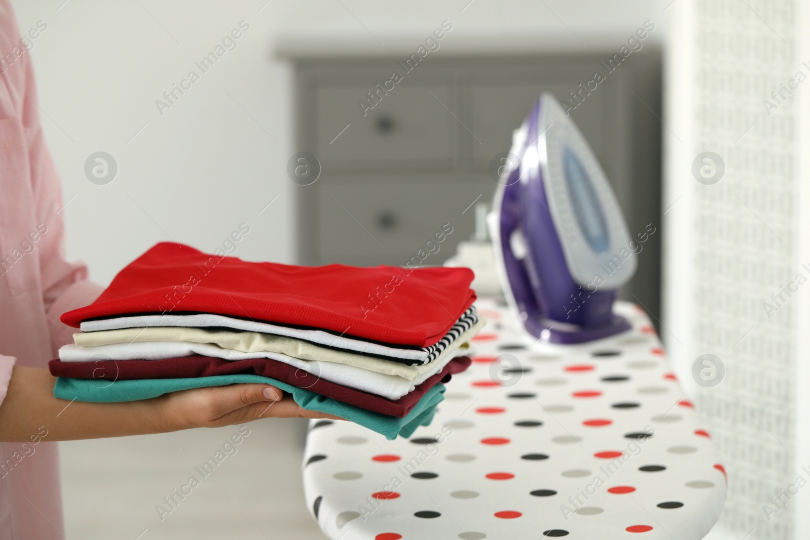 Photo of Woman with stack of freshly ironed clothes indoors, closeup