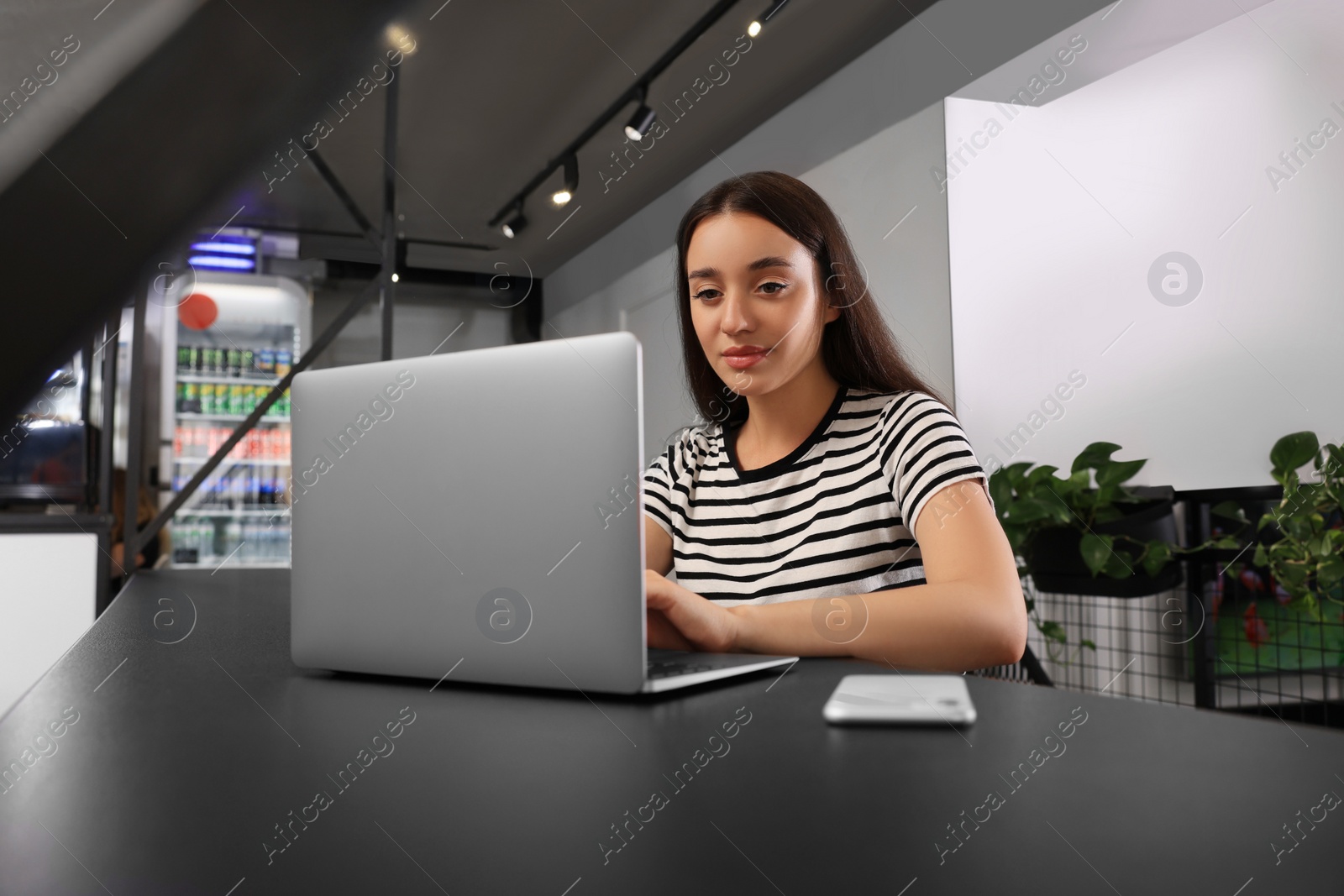 Photo of Young woman using laptop at table in hostel dining room