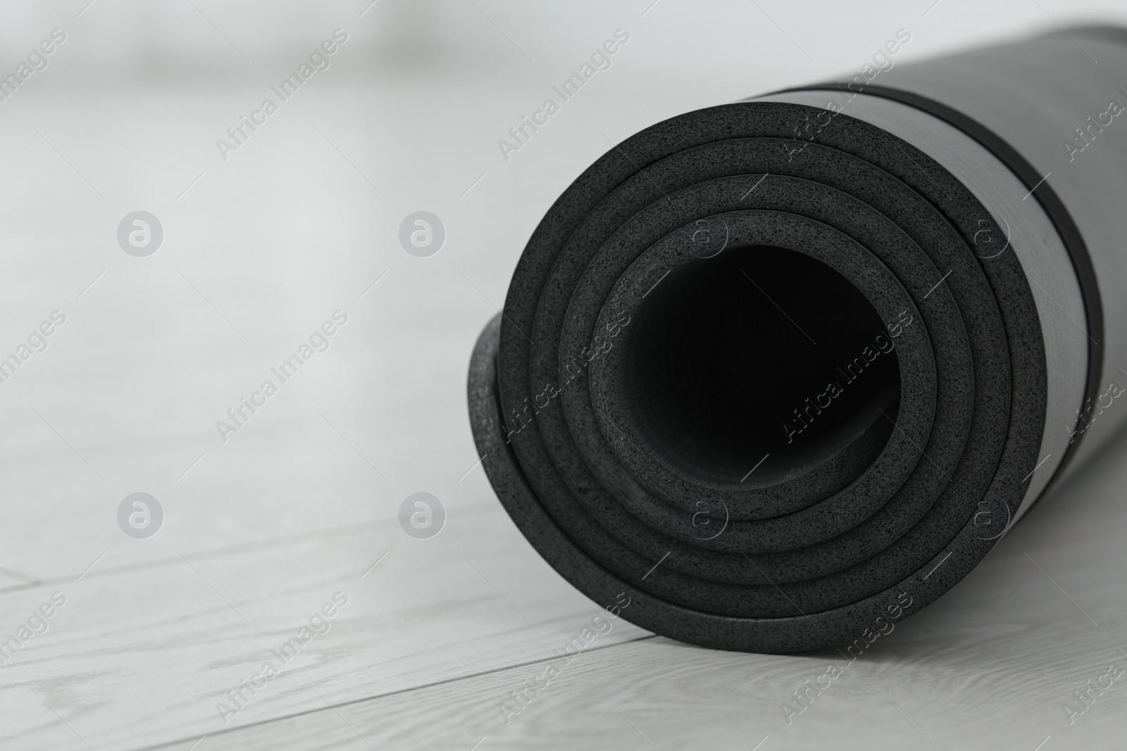 Photo of Rolled yoga mat on wooden floor, closeup. Space for text