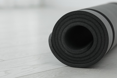 Photo of Rolled yoga mat on wooden floor, closeup. Space for text