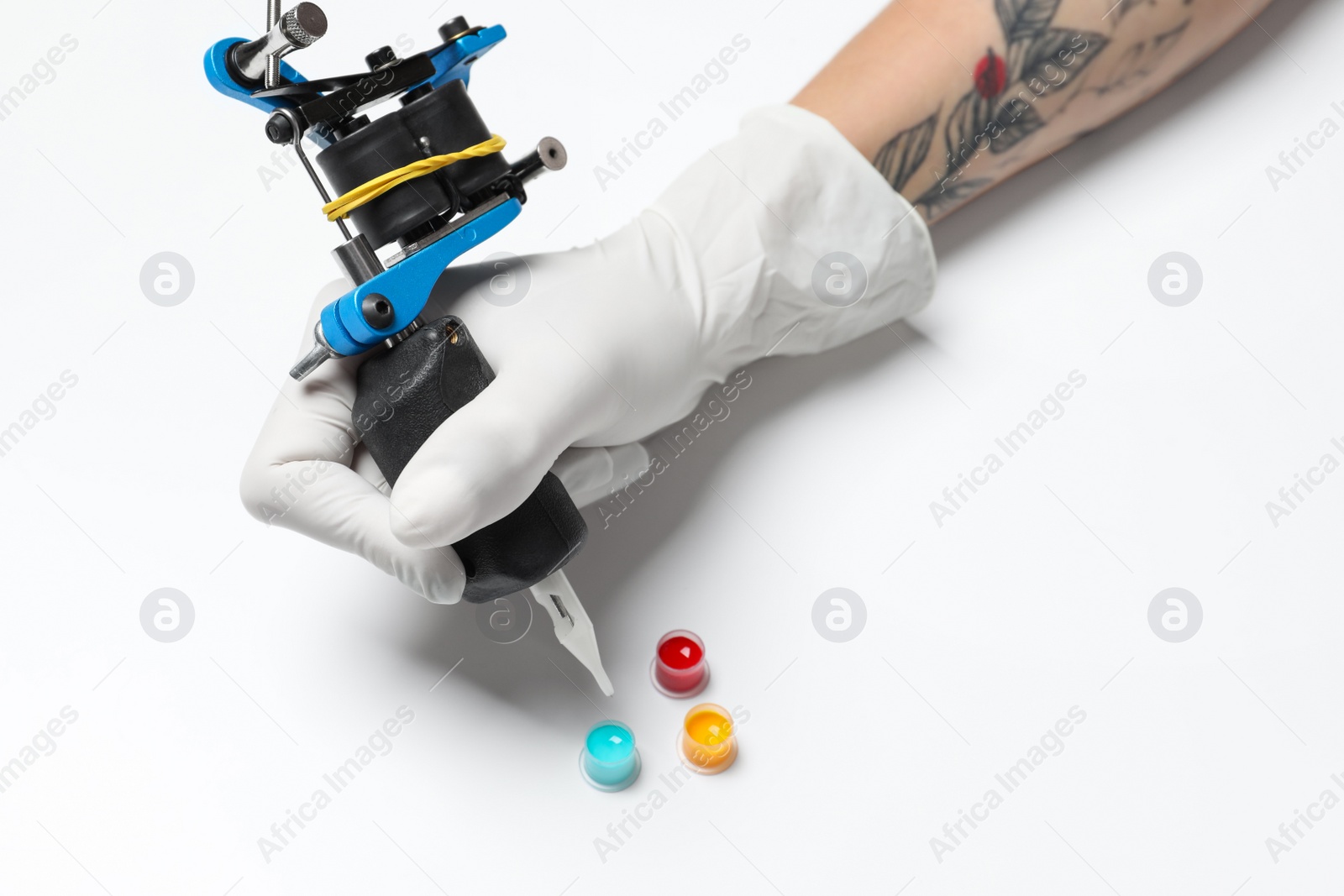 Photo of Tattoo artist with professional machine and colorful ink on white background, closeup