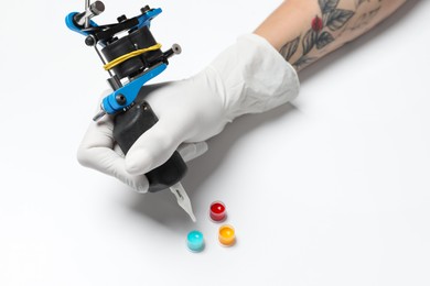 Tattoo artist with professional machine and colorful ink on white background, closeup