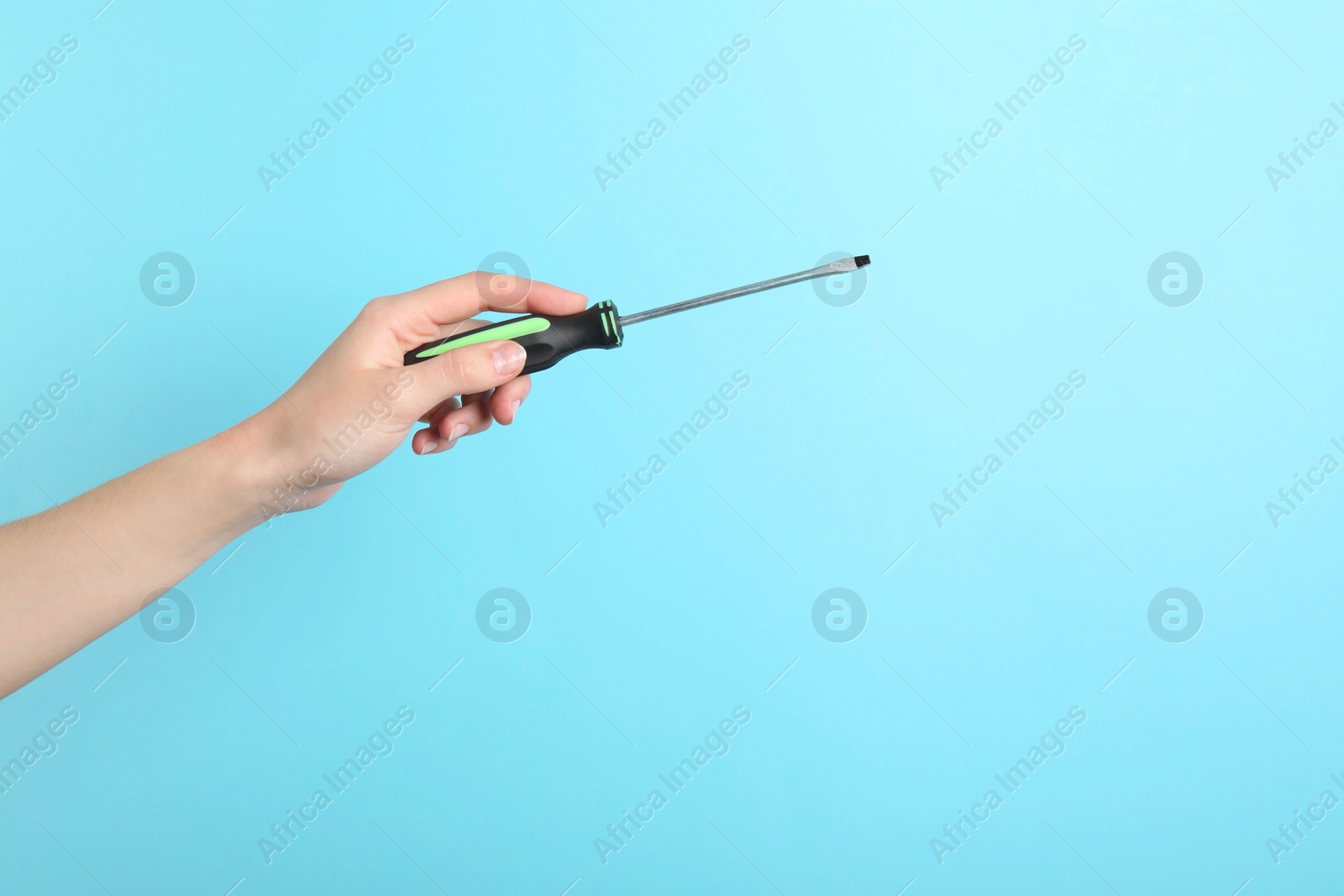 Photo of Woman holding screwdriver on light blue background, closeup. Space for text