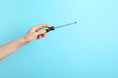 Woman holding screwdriver on light blue background, closeup. Space for text