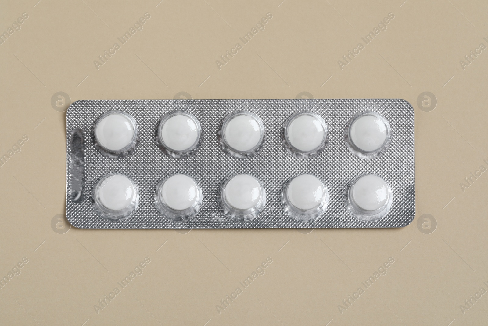 Photo of White pills in blister on beige background, top view
