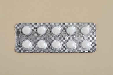Photo of White pills in blister on beige background, top view
