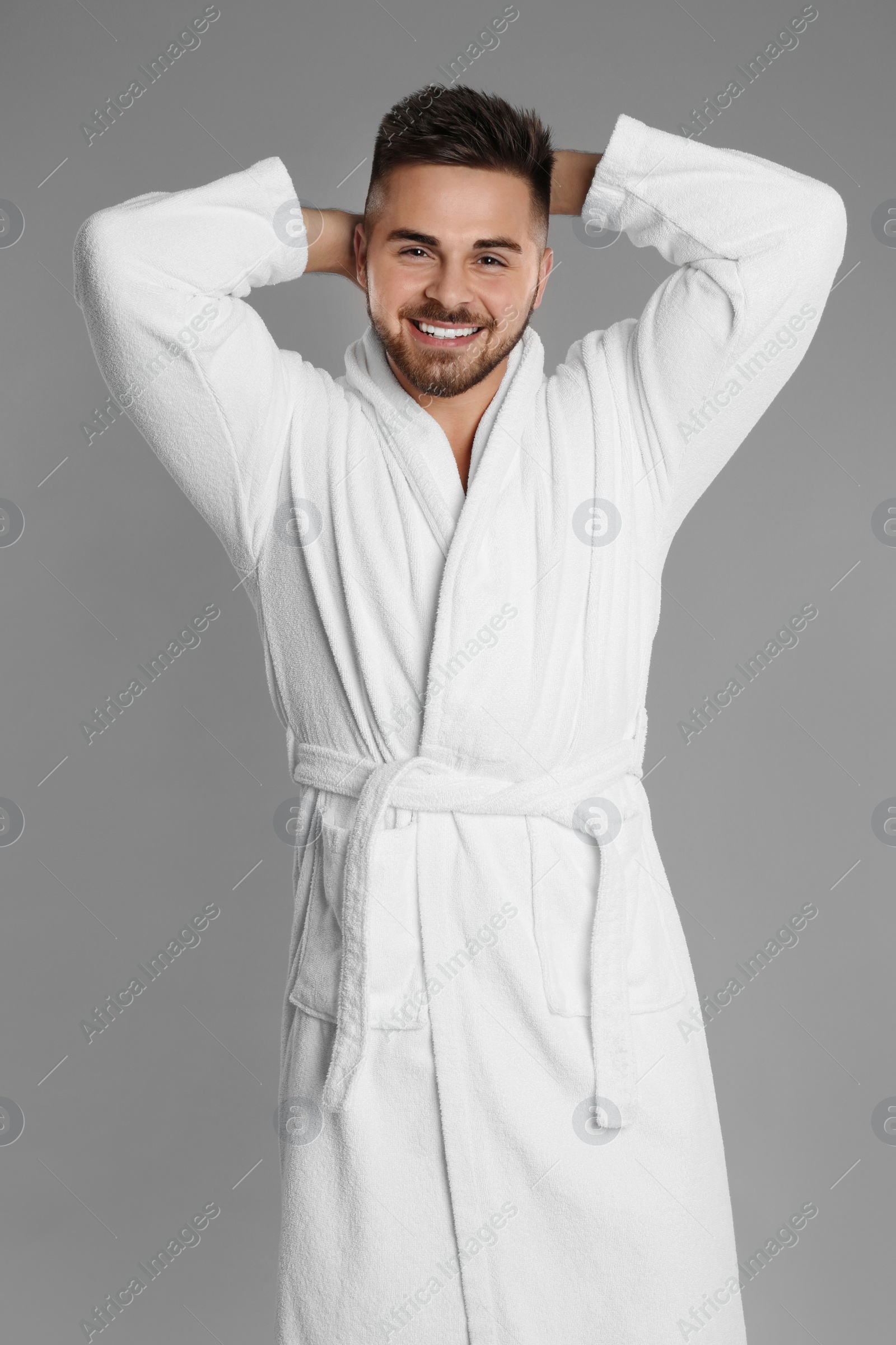 Photo of Happy young man in bathrobe on grey background