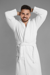 Happy young man in bathrobe on grey background