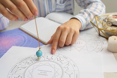 Photo of Astrologer using zodiac wheel and pendulum for fate forecast at table, closeup. Fortune telling
