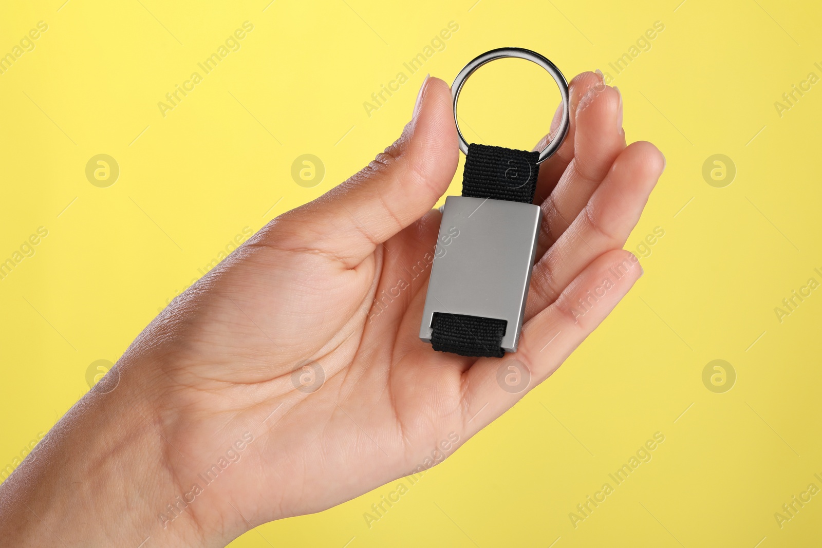 Photo of Woman holding metallic keychain on yellow background, closeup