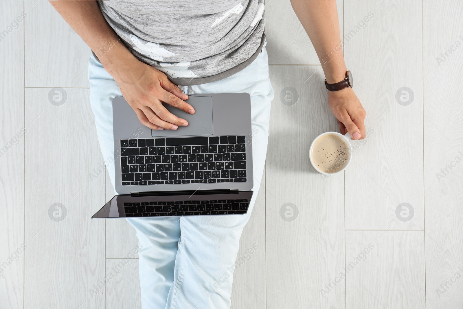 Photo of Young man with cup of coffee and laptop while sitting on floor, top view