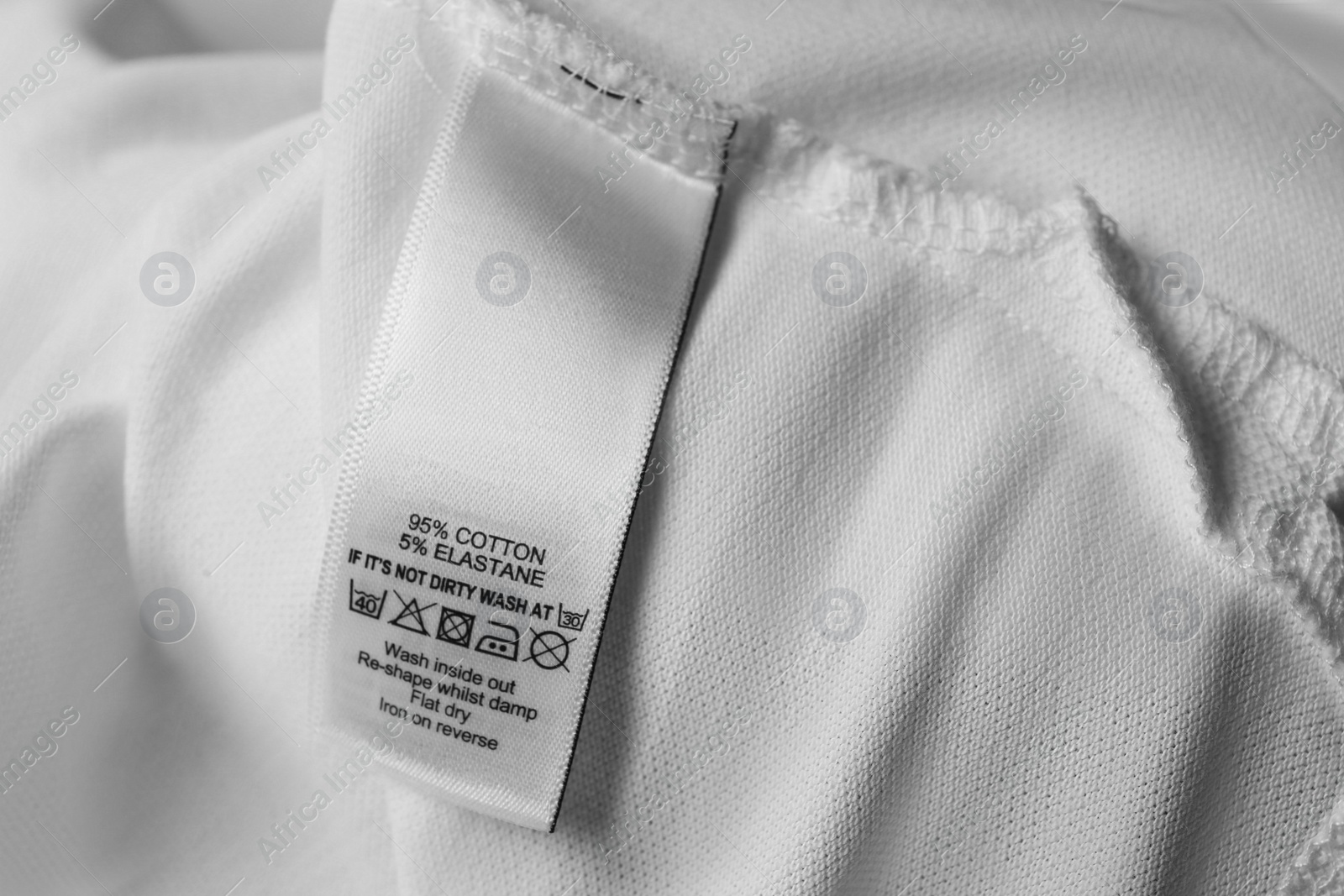 Photo of Clothing label with care symbols and material content on white shirt, closeup view