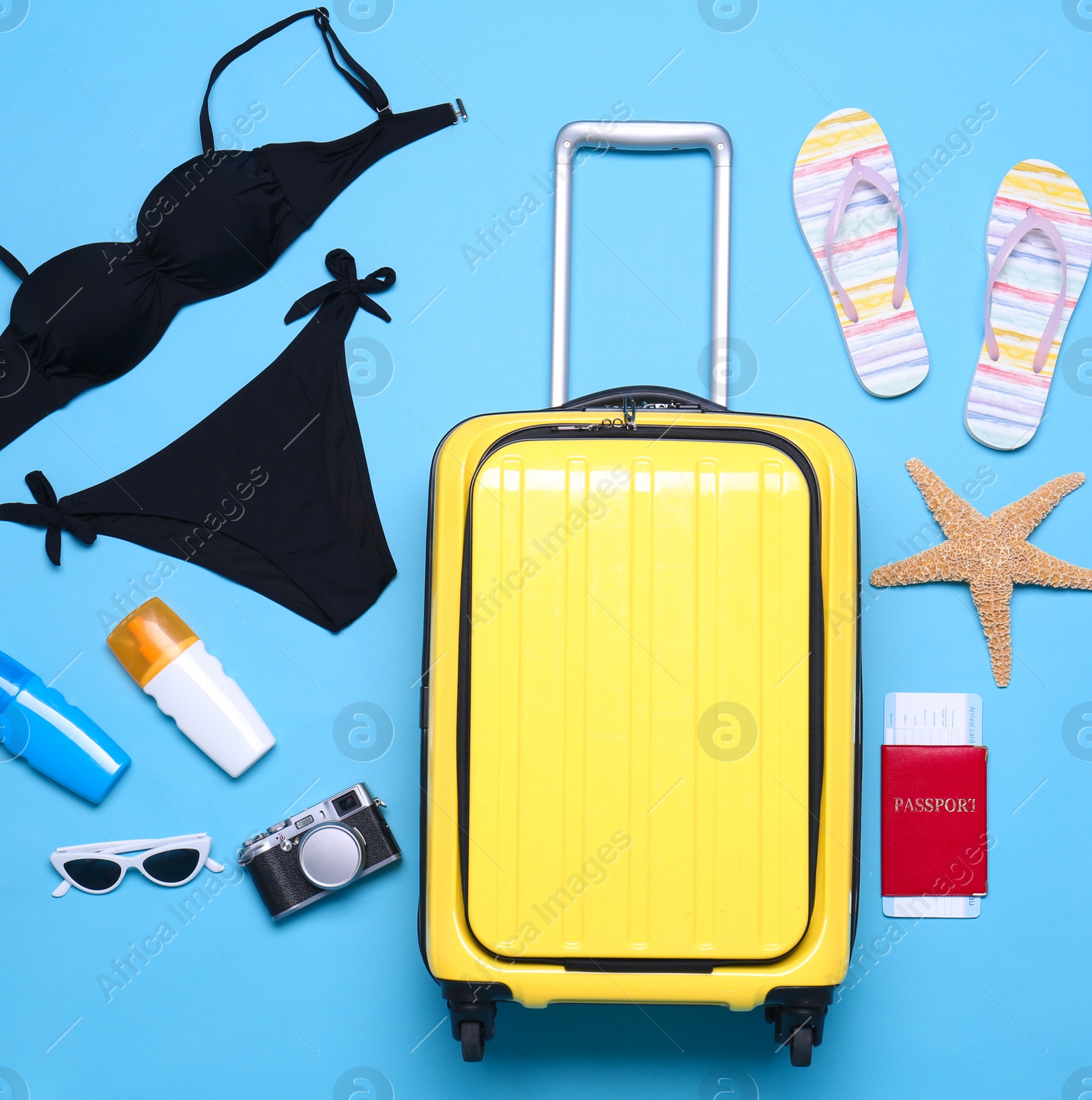 Photo of Yellow suitcase and beach objects on blue background, flat lay