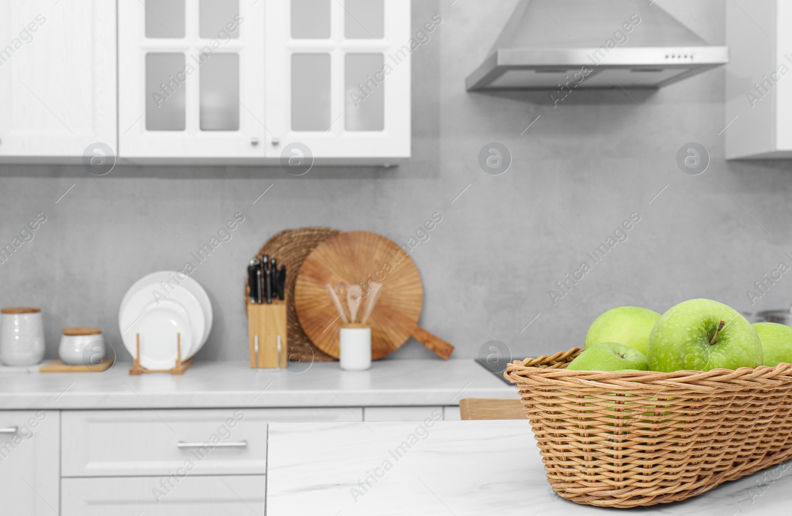 Photo of Wicker basket with ripe apples on white marble table in kitchen