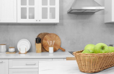 Photo of Wicker basket with ripe apples on white marble table in kitchen