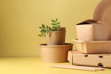 Photo of Eco friendly food packaging. Paper containers, tableware and green twigs on pale yellow background, space for text