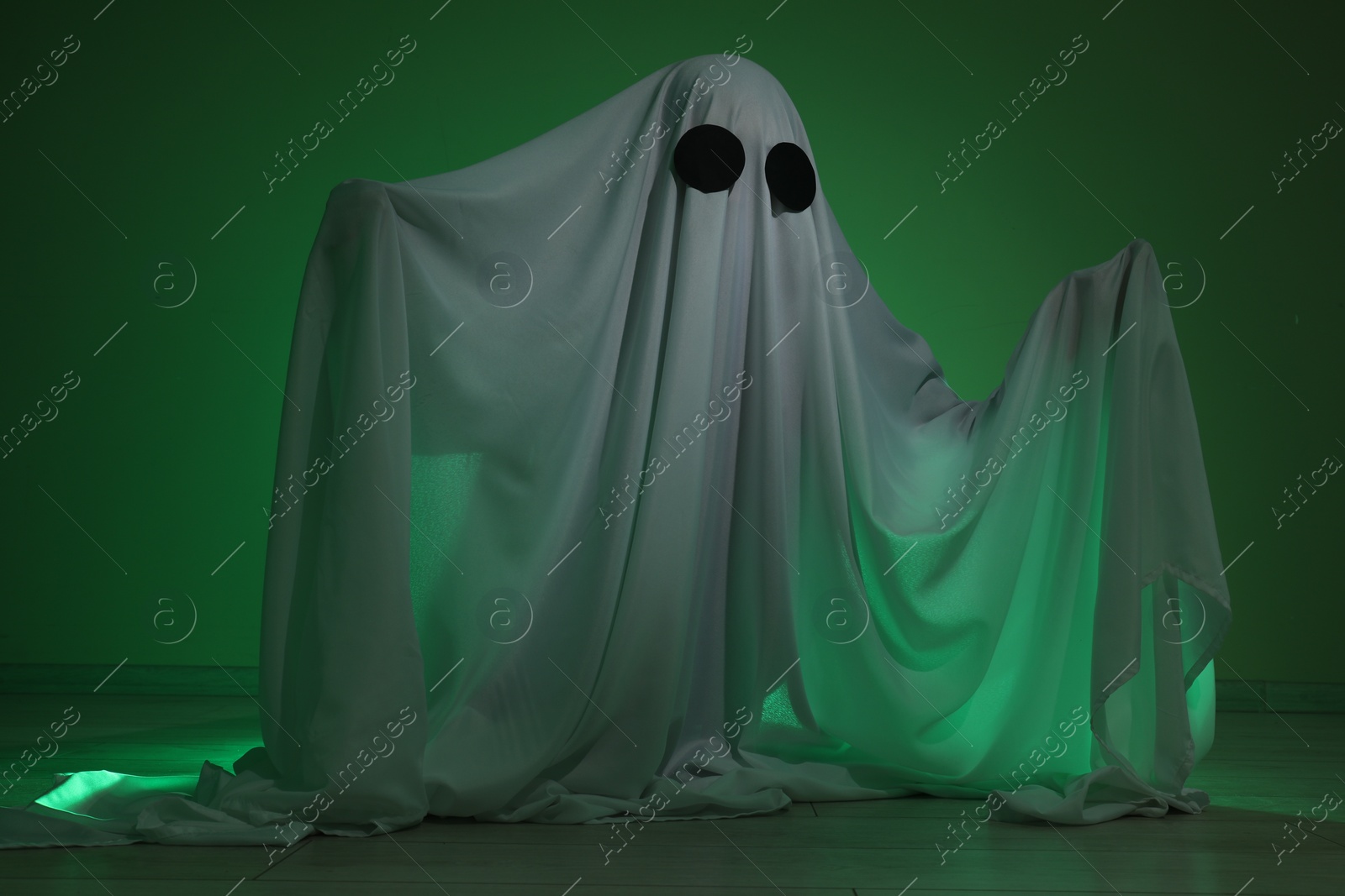 Photo of Creepy ghost. Woman covered with sheet in green light