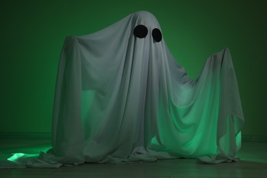 Photo of Creepy ghost. Woman covered with sheet in green light