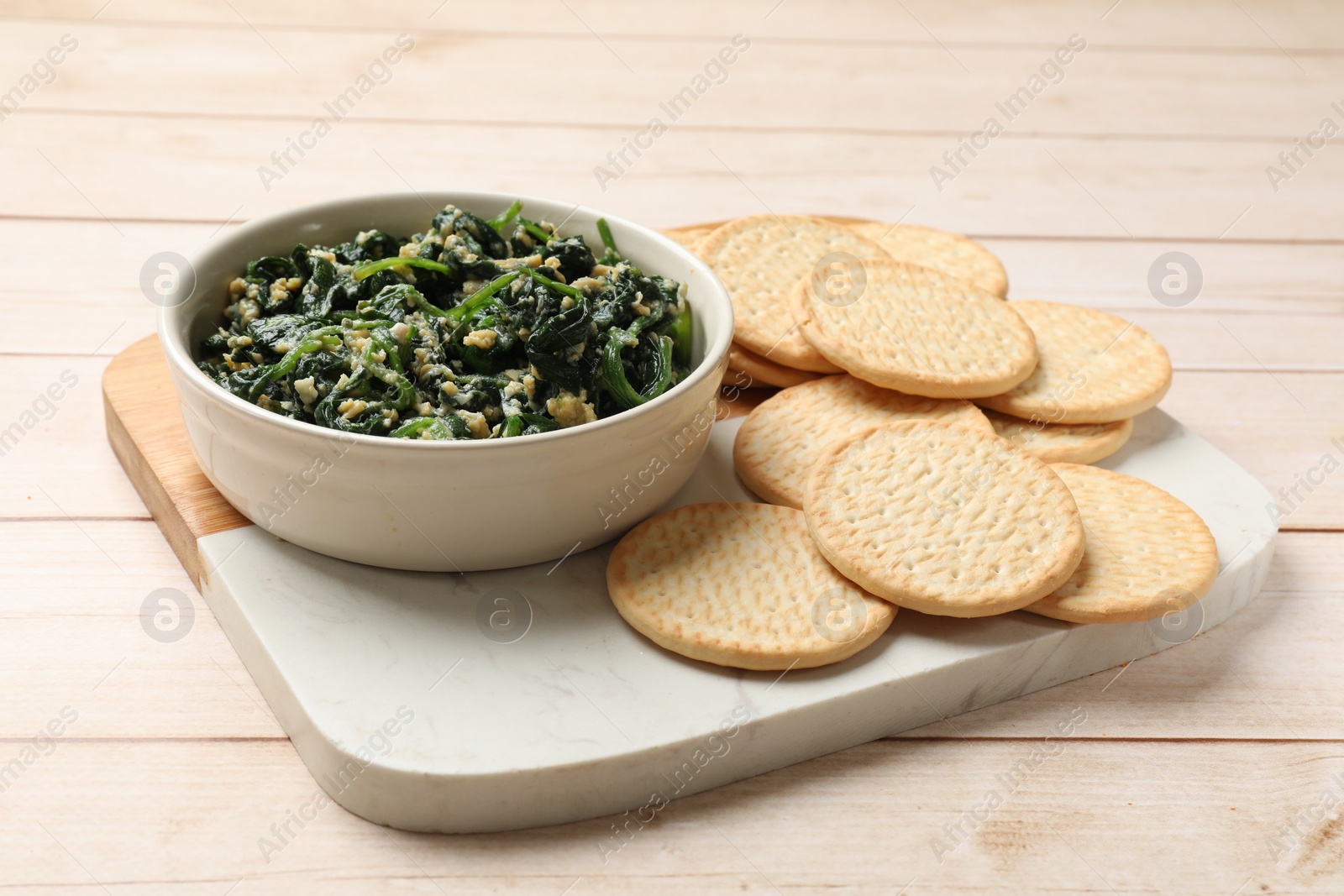 Photo of Tasty spinach dip with eggs in bowl and crackers on light wooden table