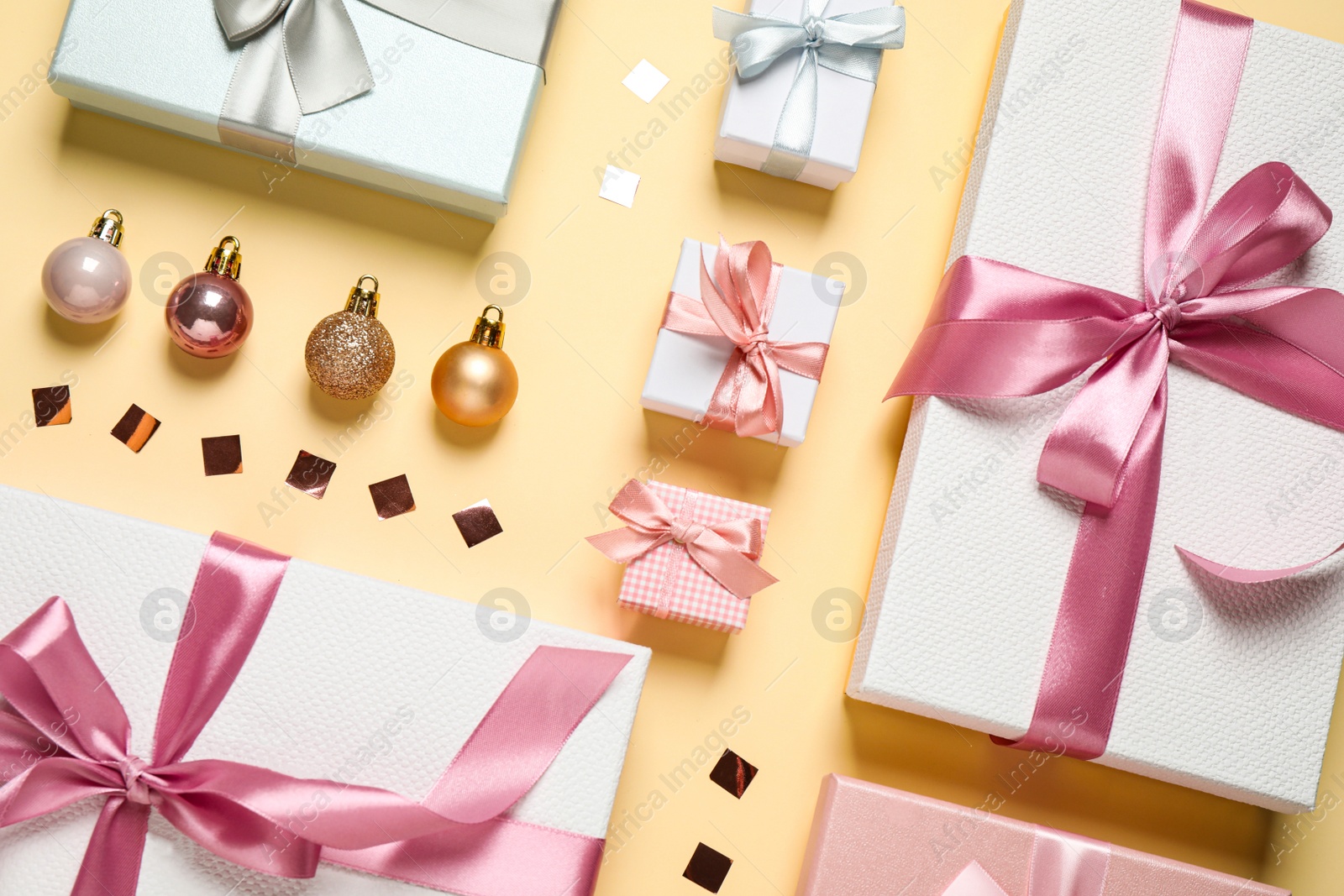 Photo of Beautiful gift boxes, Christmas balls and confetti on beige background, flat lay