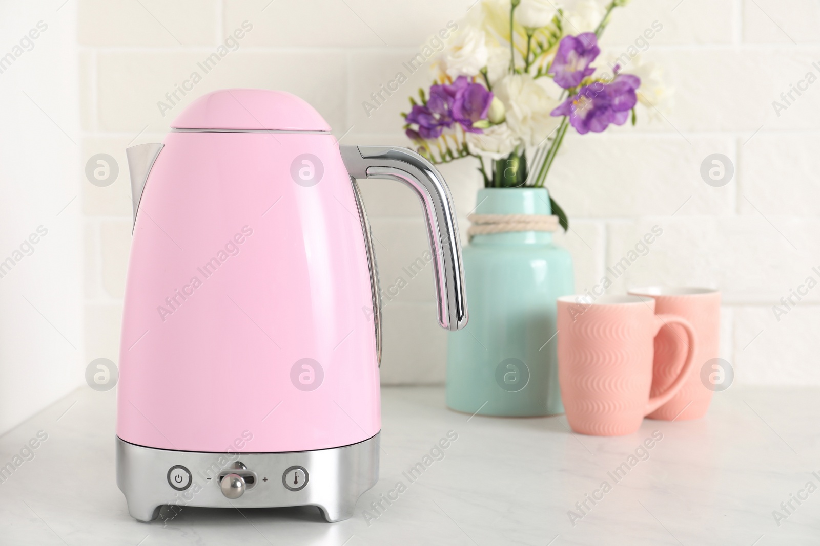 Photo of Modern electric kettle, bouquet and cups on counter in kitchen