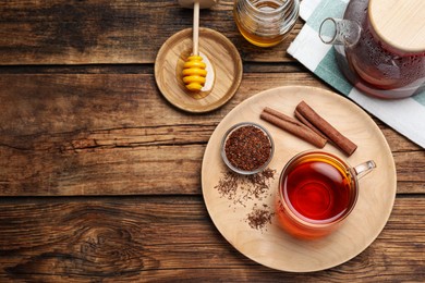 Freshly brewed rooibos tea, dry leaves and cinnamon sticks on wooden table, flat lay. Space for text