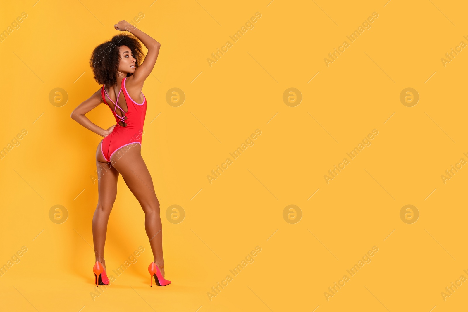 Photo of Beautiful woman in bright one-piece summer swimsuit and stylish high heel shoes on yellow background, space for text