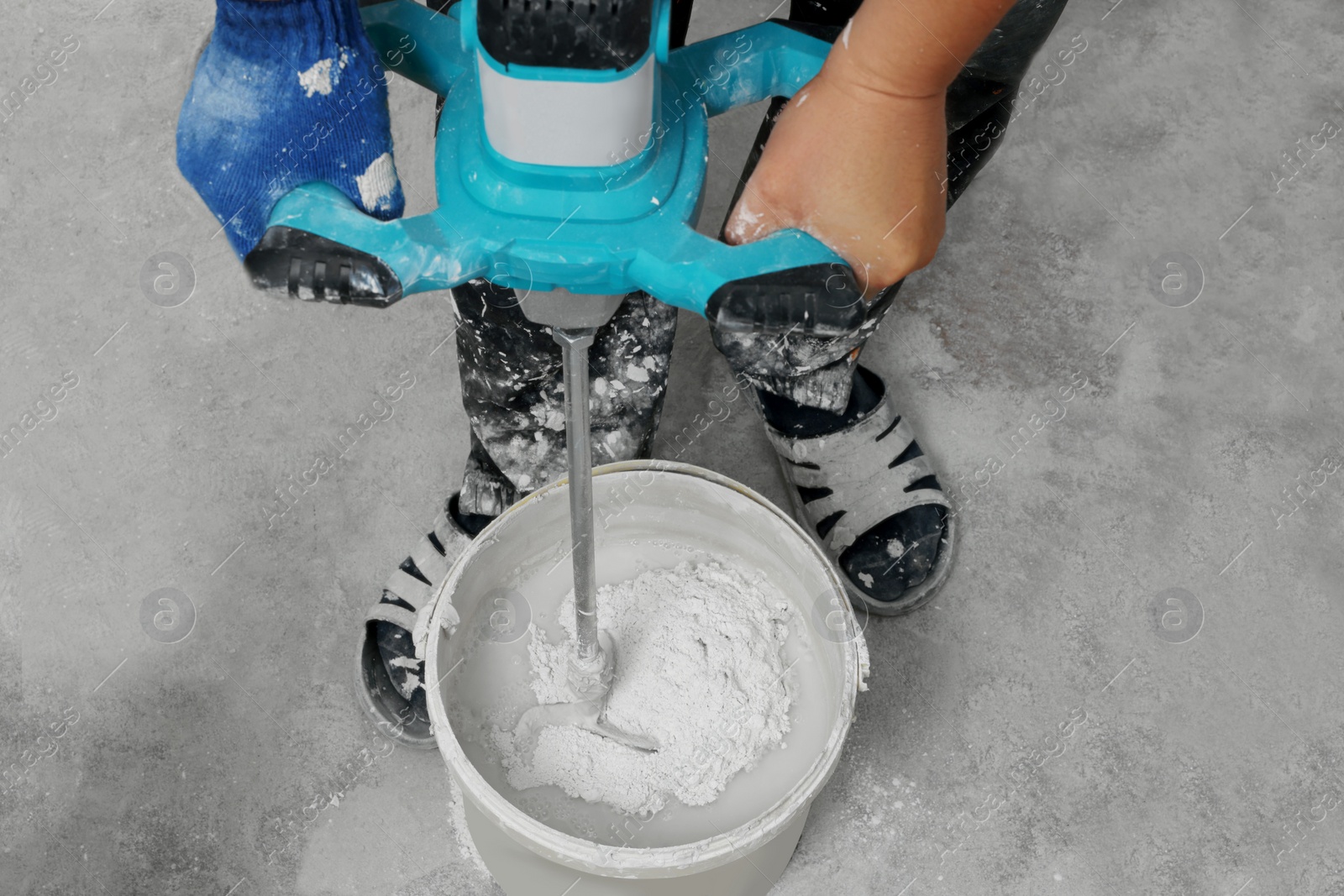 Photo of Professional worker mixing plaster in bucket indoors, closeup