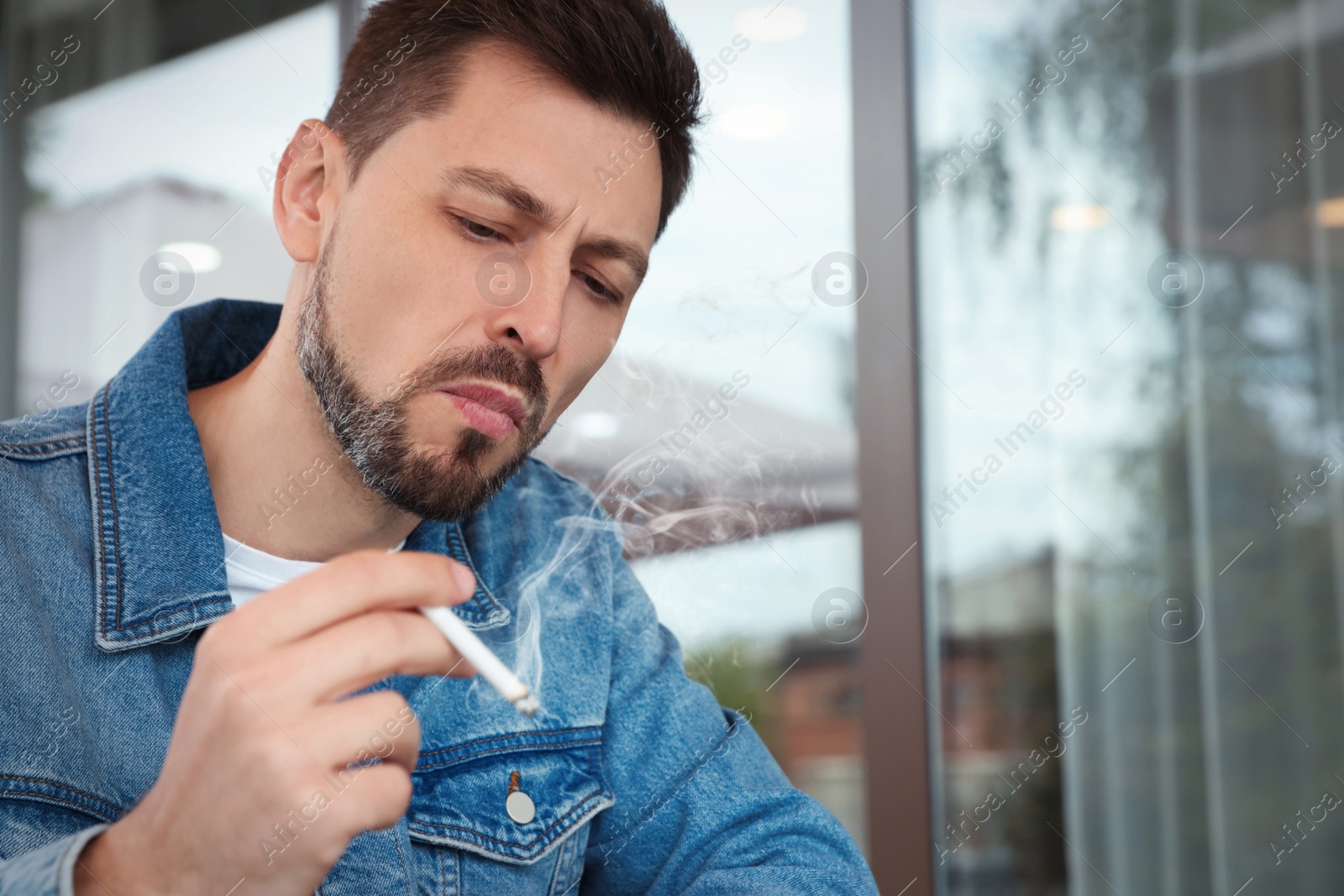 Photo of Handsome man smoking cigarette outdoors. Space for text