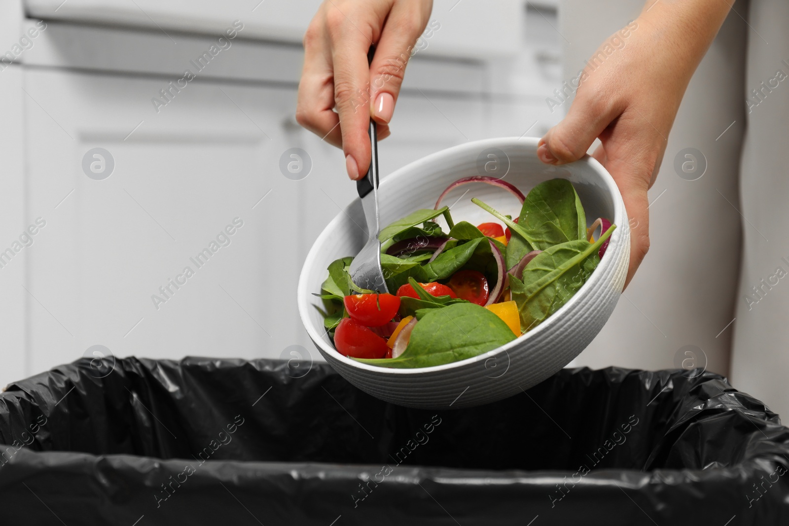 Photo of Woman throwing vegetable salad into bin indoors, closeup