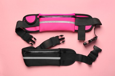 Stylish waist bags on pink background, flat lay
