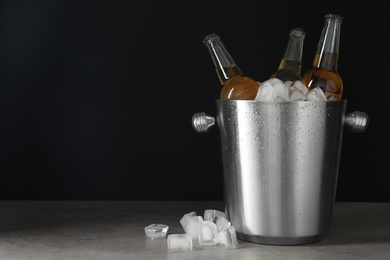 Photo of Metal bucket with bottles of beer and ice cubes on grey table. Space for text