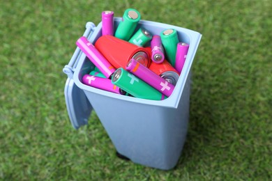 Photo of Many used batteries in recycling bin on green grass